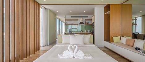 A modern hotel room with a large bed, a wooden partition, a sofa, and a view of the kitchen.