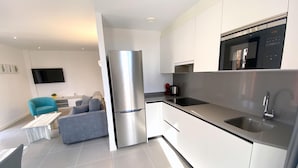 A modern kitchen with a stainless steel refrigerator, a built-in oven, and a microwave. There is a dining area with a grey sofa and a small table. - Modern apartment with air conditioning in Castelló d'Empúries (Castelló d'Empúries)