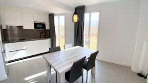 A modern kitchen with white cabinets, a black countertop, and a built-in microwave. There is a dining area with a white table and four chairs. - Modern apartment with air conditioning in Castelló d'Empúries (Castelló d'Empúries)