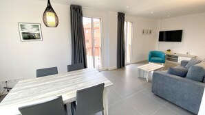 A modern living room with a dining area, grey sofas, a blue armchair, a flat-screen TV, and a large window with curtains. - Modern apartment with air conditioning in Castelló d'Empúries (Castelló d'Empúries)