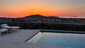 A pool area with lounge chairs and a view of a sunset over a mountainous landscape. - Sunrise Villa Sea View up to 4 pax (Ano Mera)