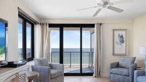 Een moderne woonkamer met een grote televisie, twee fauteuils met een patroon, een ronde salontafel en een balkon met uitzicht op de oceaan.