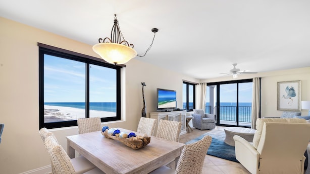 Een ruime woonkamer met een grote eettafel, rieten stoelen, een televisie en uitzicht op de oceaan.