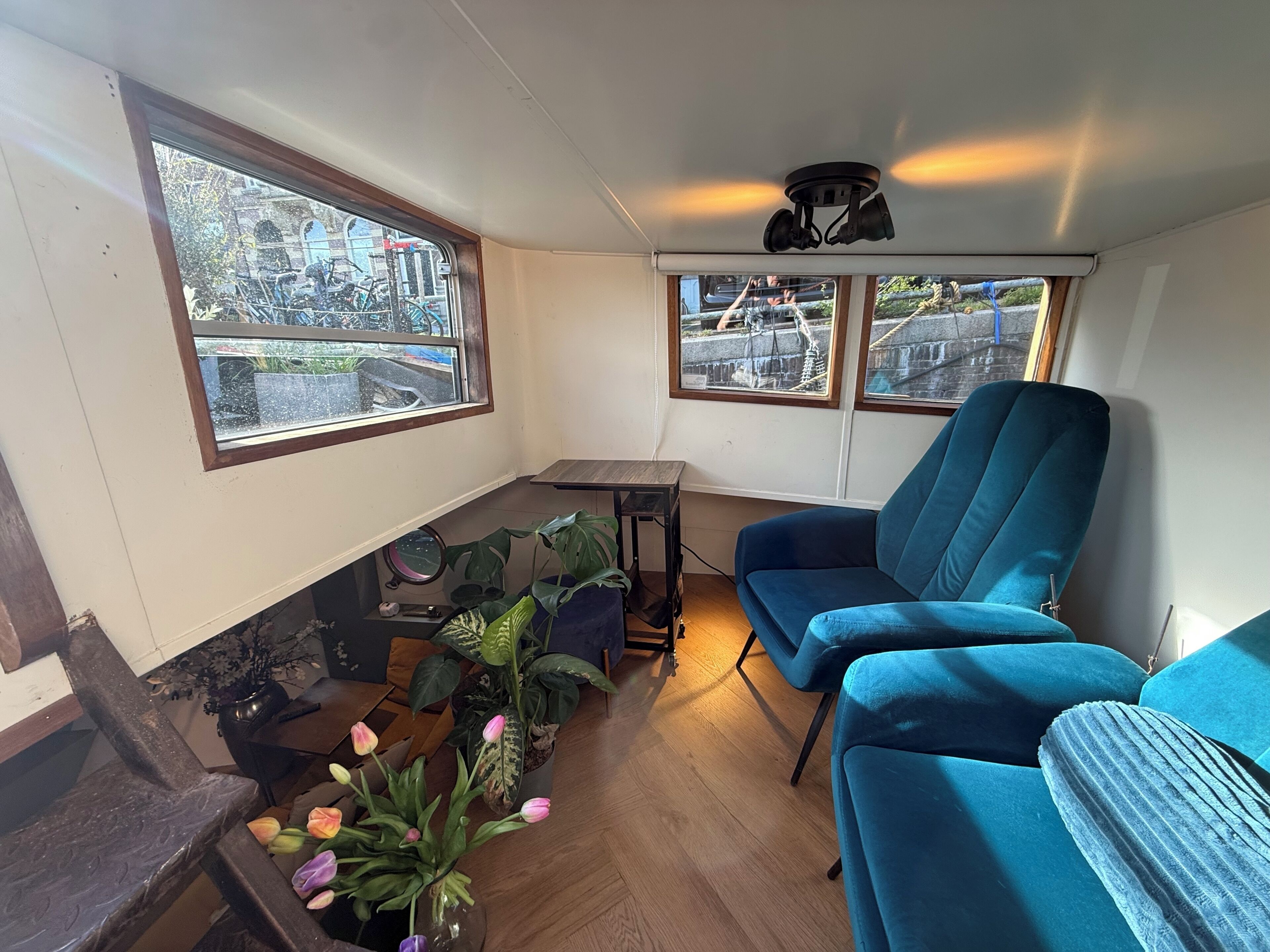 Ein Zimmer mit einem blauen Sofa, einem kleinen Tisch, einer Zimmerpflanze und Blick auf Fahrräder draußen.