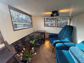 Une pièce avec un canapé bleu, une petite table, une plante en pot et une vue sur les vélos garés à l’extérieur.
