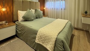 Moderni makuuhuone, jossa on suuri sänky, yöpöydät, yölamppu ja ikkuna, jossa on verhot.