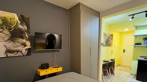 Ett hotellrum med en säng, en tv som är monterad på väggen, ett litet skrivbord med en lampa och en tavla.