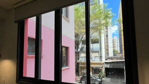 Ett fönster med utsikt över en gata, en rosa byggnad och en gul soffa.