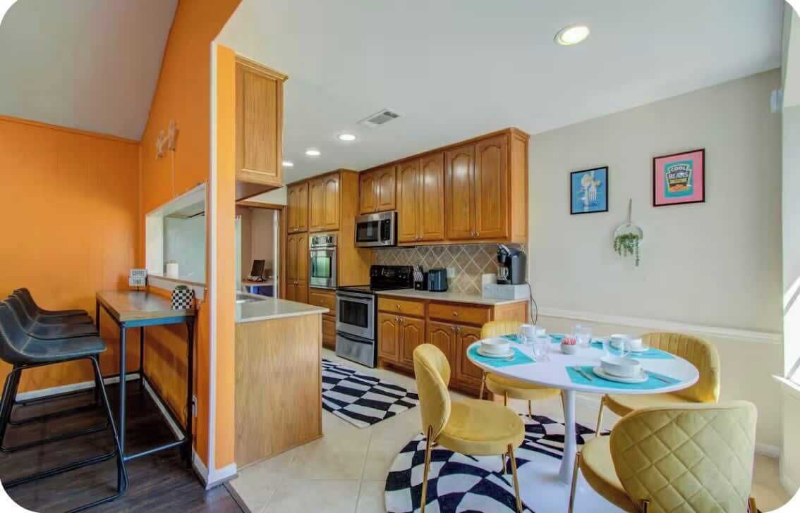 A compact kitchen with wooden cabinets, a microwave, and a coffee machine. There is a dining area with a round table and chairs.