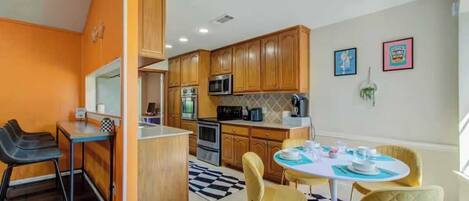A compact kitchen with wooden cabinets, a microwave, and a coffee machine. There is a dining area with a round table and chairs.