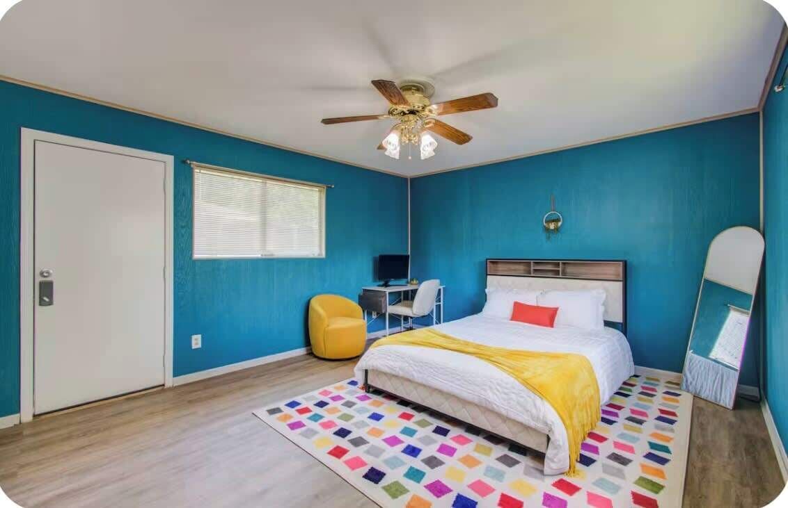 A bedroom with a bed, a ceiling fan, a desk, a chair, and a window.