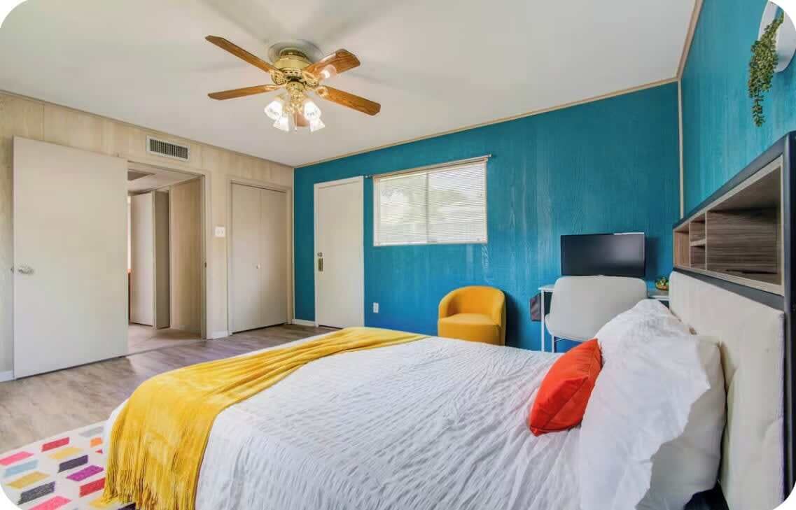 A bedroom with a bed, a ceiling fan, a window, and a chair.