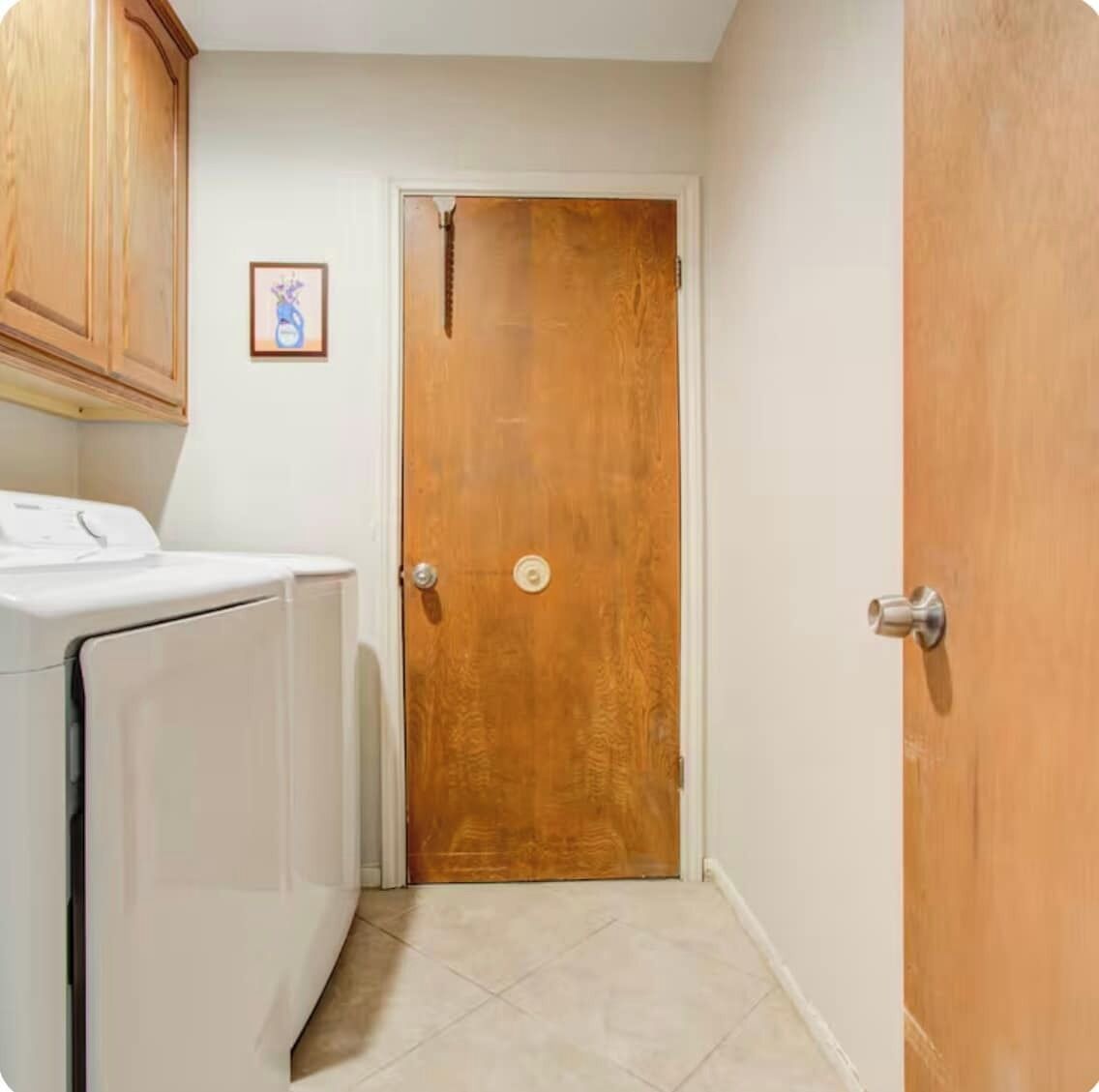 A laundry room with a washing machine, a wooden door, and a small framed picture on the wall.