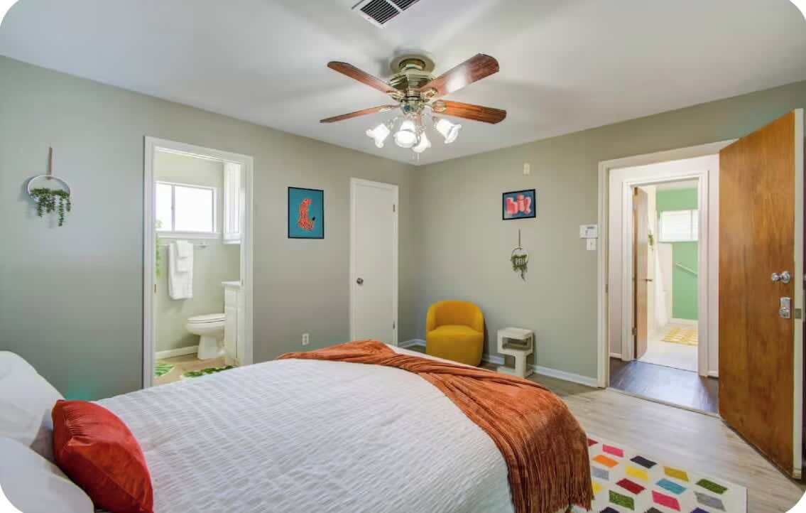 A bedroom with a bed, a ceiling fan, a chair, and a door leading to another room.