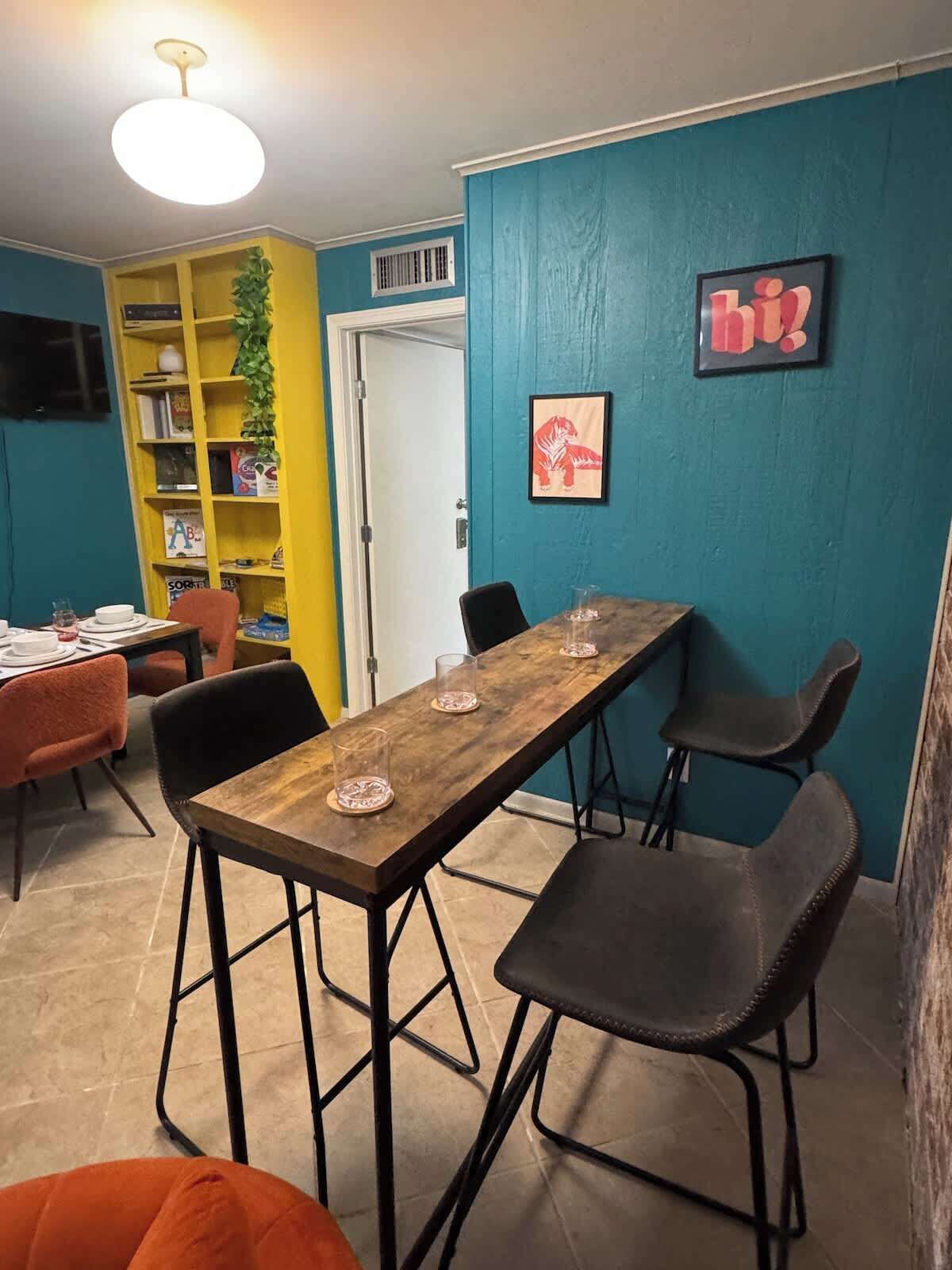 Un comedor con una mesa de madera, sillas negras y una estantería con libros y adornos.
