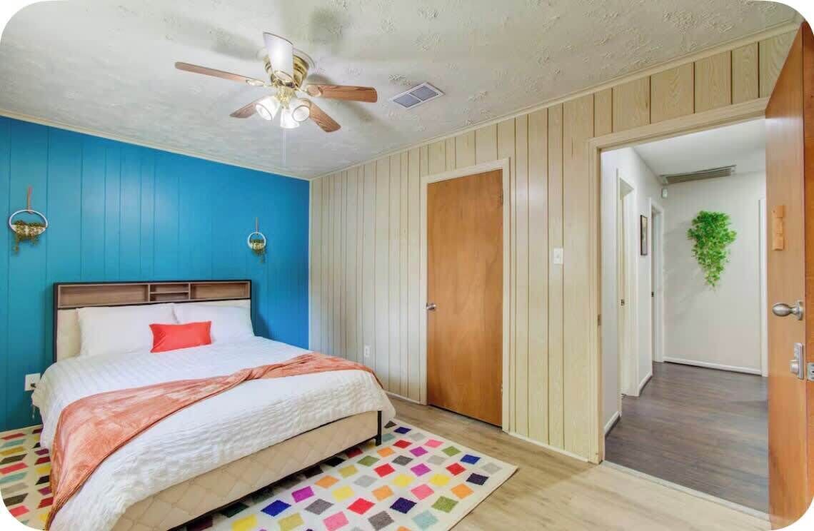 Une chambre à coucher avec un lit, un ventilateur de plafond, une porte en bois et un tapis coloré.