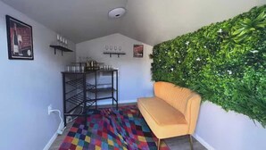 Ein Zimmer mit einem farbenfrohen Schachbrettteppich, einer Couch, einer an der Wand befestigten Zimmerpflanze und einem Metallregal mit Gegenständen darauf.