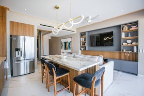 A modern kitchen with a central island, bar stools, a built-in refrigerator, and a flat-screen TV mounted on the wall. - Romantic Zone Retreat w/ Rooftop Pool + Epic Views (Puerto Vallarta)