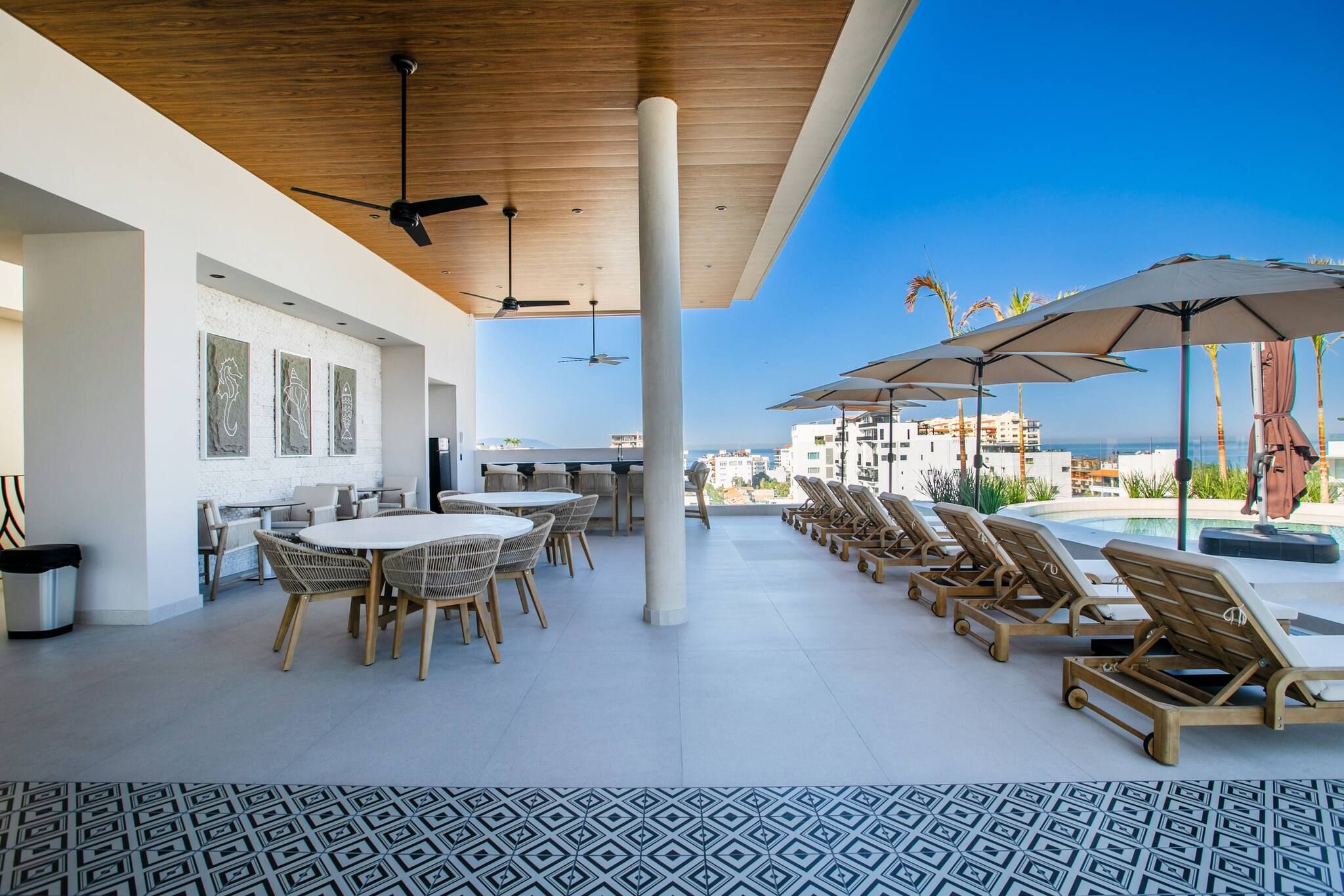 A rooftop terrace with a pool, lounge chairs, a dining area, and a view of the city.