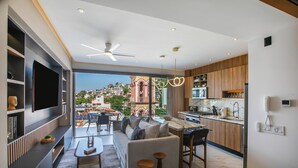 Uma sala de estar moderna com sofá, mesa de centro e TV, integrada a uma cozinha com armários de madeira e um espaço para refeições.