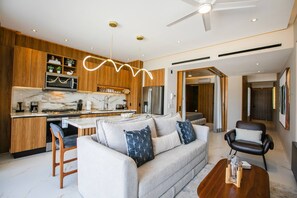 A modern kitchen with a central island, wooden cabinets, and a dining area with a sofa and chairs. - Romantic Zone Retreat w/ Rooftop Pool + Epic Views (Puerto Vallarta)