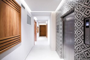 A modern hotel corridor with wooden paneling on one side, a patterned wall on the other, and a visible elevator. - Romantic Zone Retreat w/ Rooftop Pool + Epic Views (Puerto Vallarta)