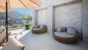 Uma área de estar moderna ao ar livre, com sofás de vime e um guarda-sol grande, com vista para a cidade.