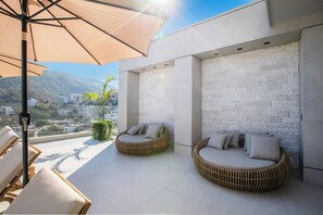 Eine Dachterrasse mit zwei Korbschaukeln, einem großen Sonnenschirm und Blick auf Stadt und Berge.