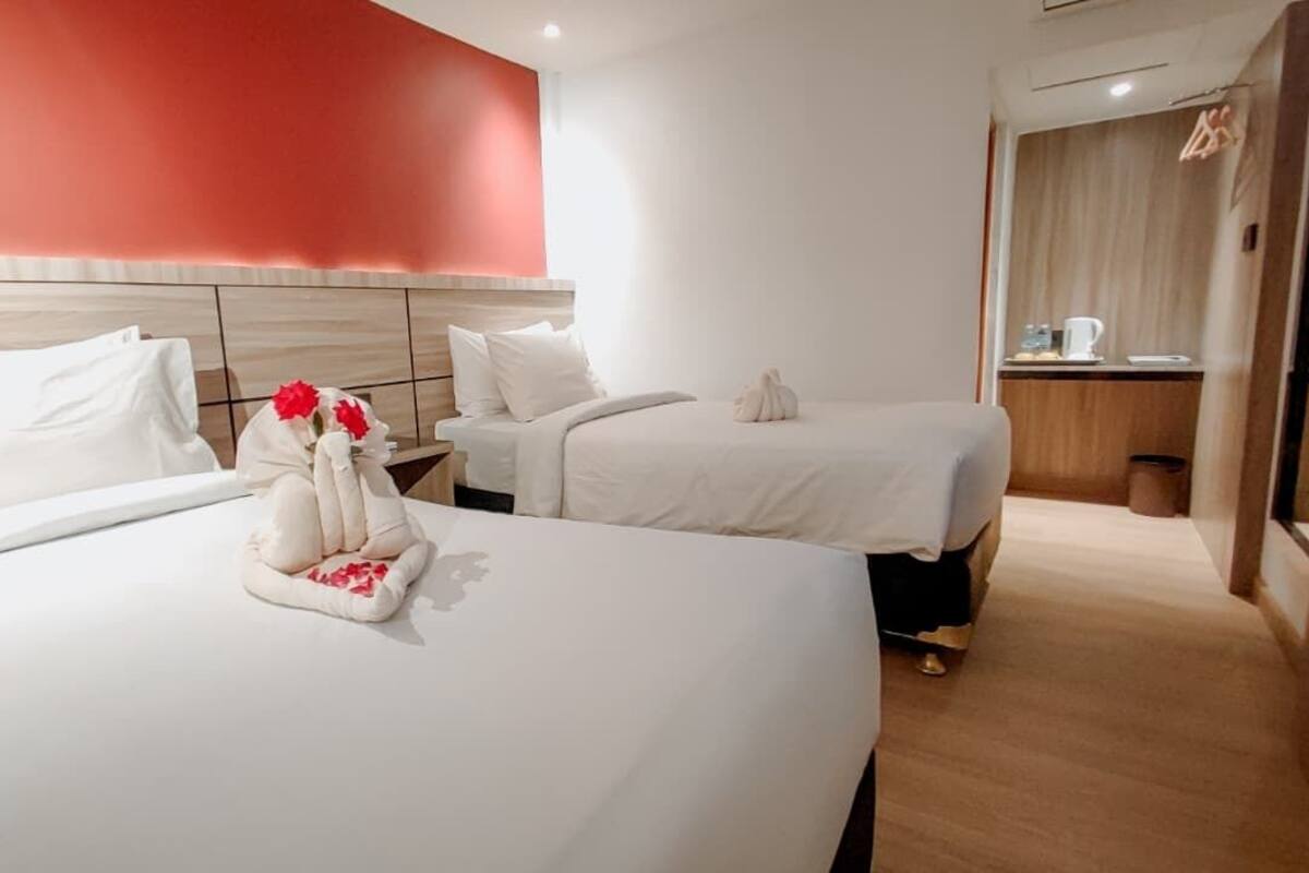A hotel room with two beds, a red accent wall, and a small kitchenette area.