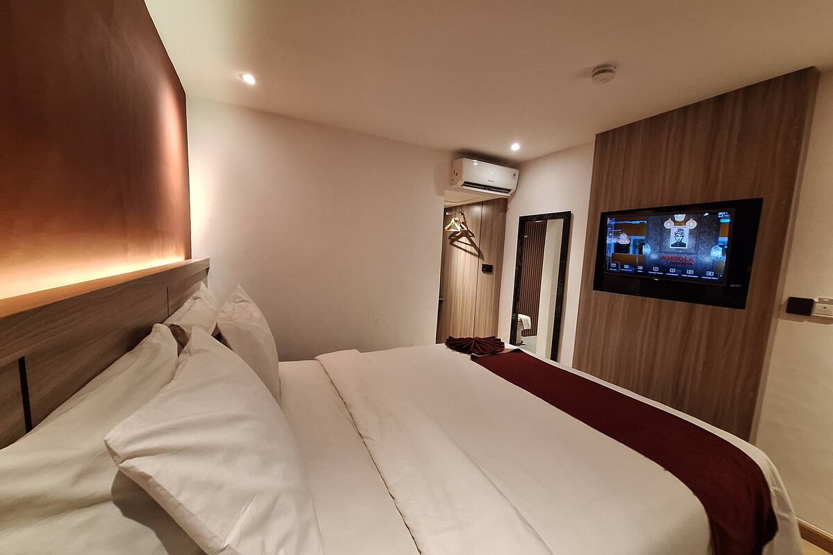 A hotel room with a large bed, a flat-screen TV mounted on the wall, and an air conditioning unit above the door.