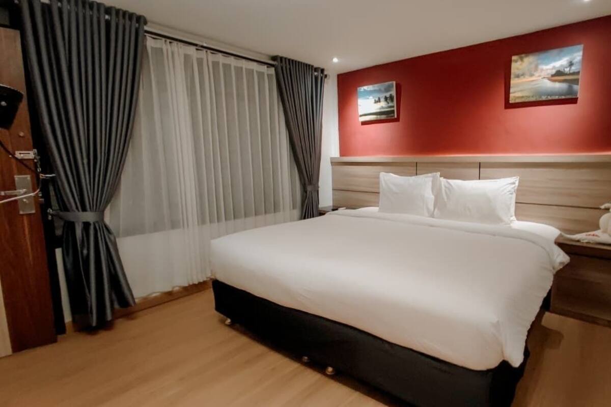 A hotel room with a large bed, wooden headboard, two paintings on the wall, and a nightstand with a telephone.