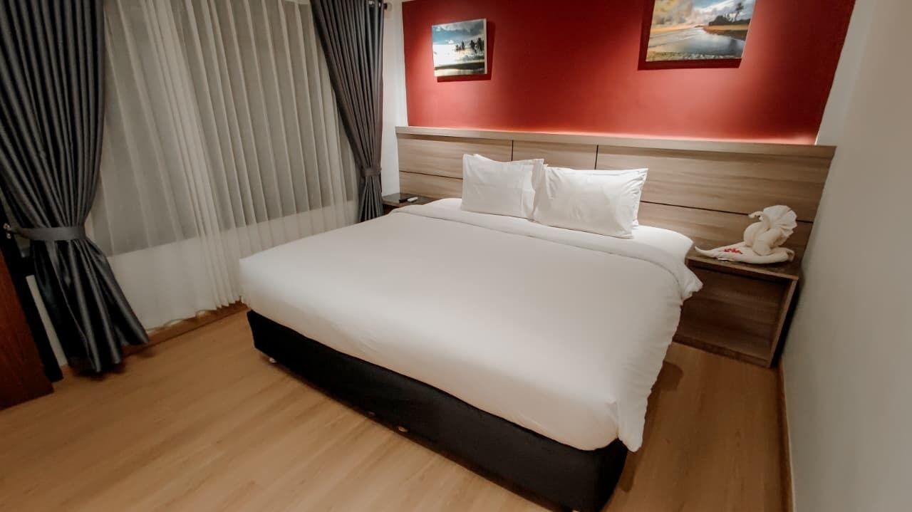 Une chambre d’hôtel avec un grand lit, une tête de lit en bois et deux tableaux accrochés au mur.
