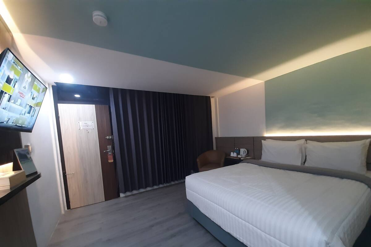 A hotel room with a large bed, a desk with a flat-screen TV, a chair, and a nightstand with a coffee maker.