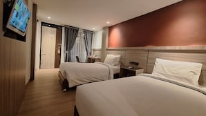 A hotel room with two beds, a TV mounted on the wall, a desk with a chair, and a window with curtains.