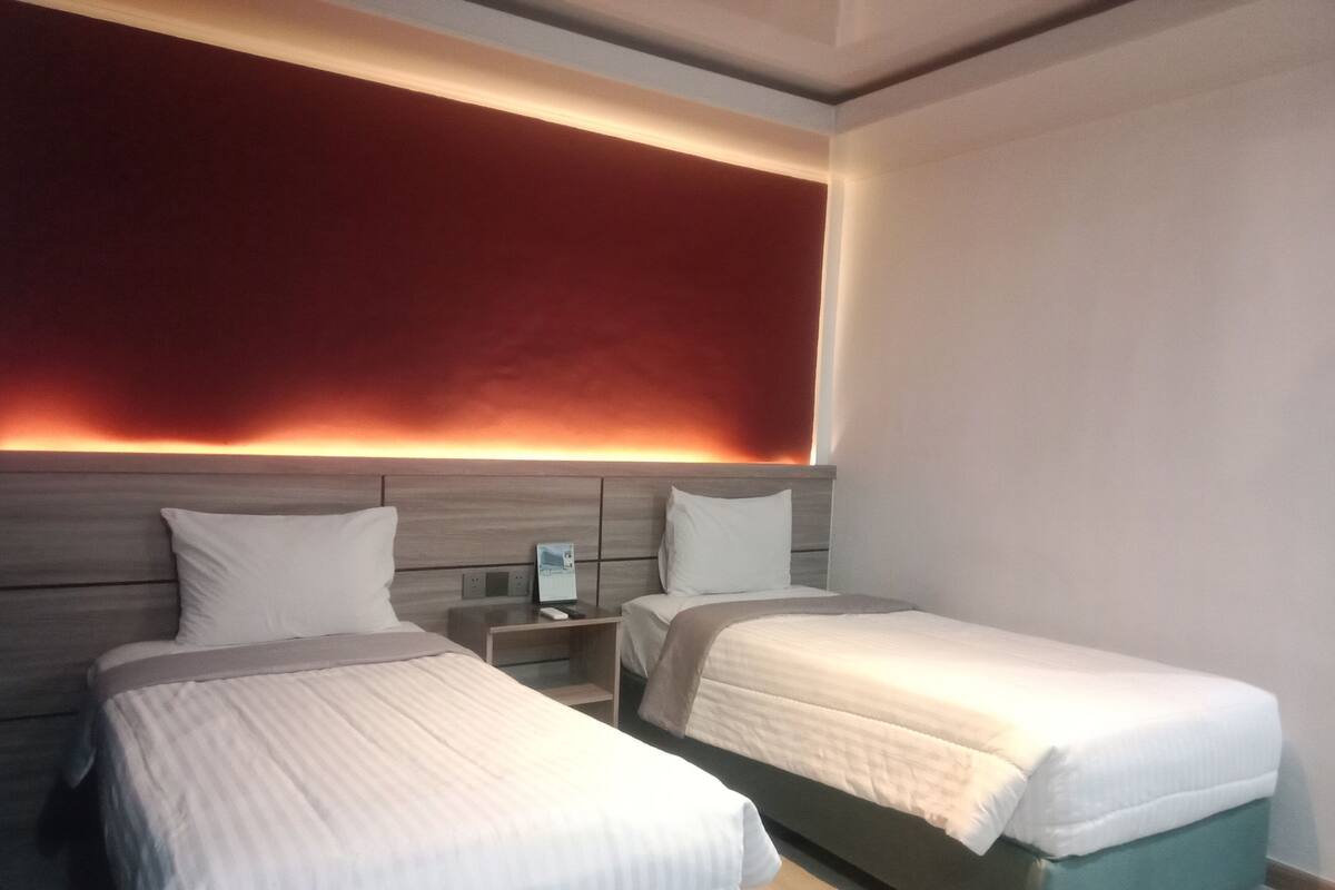 A hotel room with two beds, a nightstand, and a red accent wall.