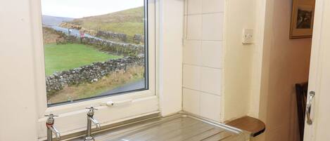 A kitchen with a sink, a window with a view of a stone wall and greenery, and a door leading to another room.