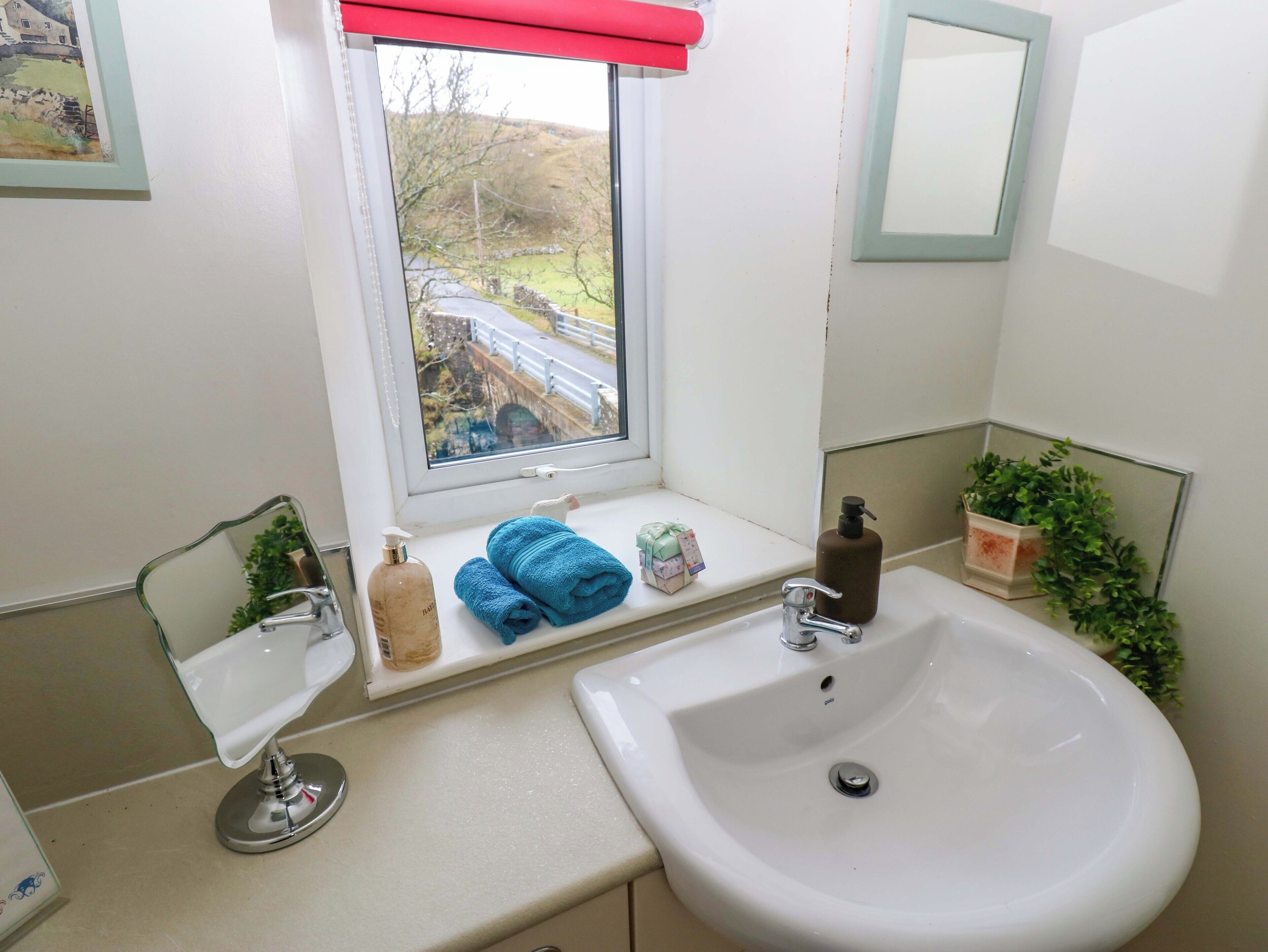 Un baño con ventana, un lavabo, un espejo y un estante con artículos de aseo.