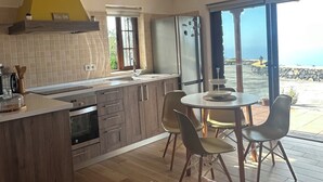 A modern kitchen with a built-in oven, a dining area with a table and chairs, and a view of the sea through large windows. - Peaceful Sea View Holiday Home with Stunning Sunsets". (Los Llanos De Aridane)