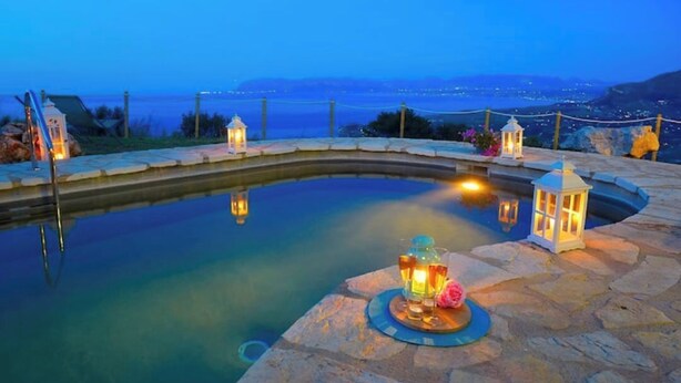 Una piscina de piedra con vista al mar, rodeada de farolillos y una barandilla de cuerda.