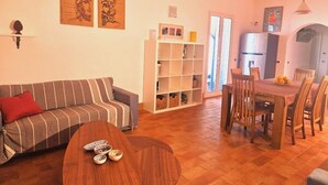 Una sala de estar con sofá, una mesa de comedor con sillas, una estantería y obras de arte en las paredes.
