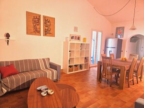 Ein Wohnzimmer mit einer Couch, einem Esstisch mit Stühlen, einem Bücherregal und Kunstwerken an den Wänden.