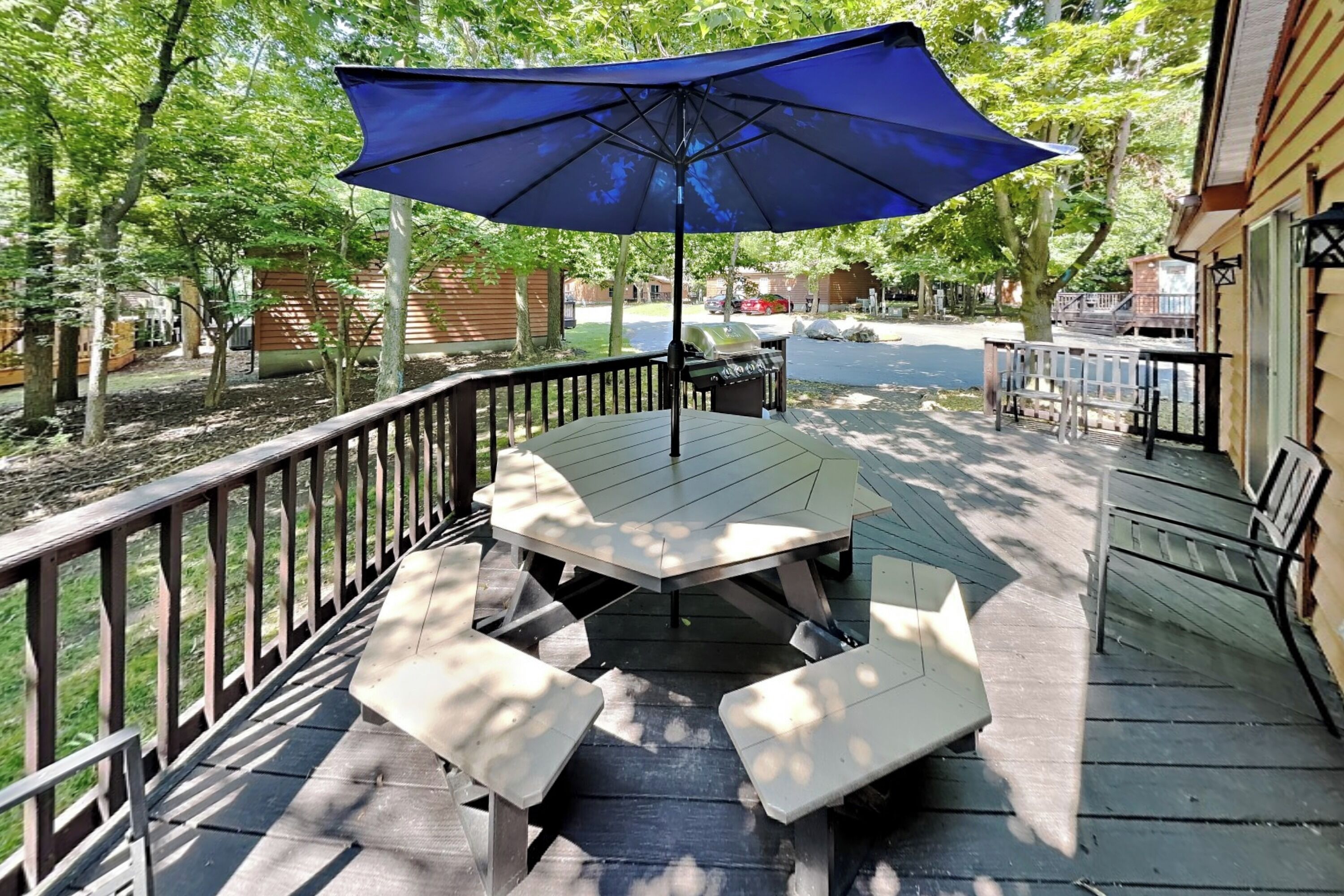 A wooden deck with a table and benches, a blue umbrella, and a barbecue grill.