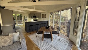 Une cuisine moderne dotée d’un îlot central, de tabourets de bar et d’une table à manger avec des chaises. Une grande fenêtre offre une vue sur l’extérieur.
