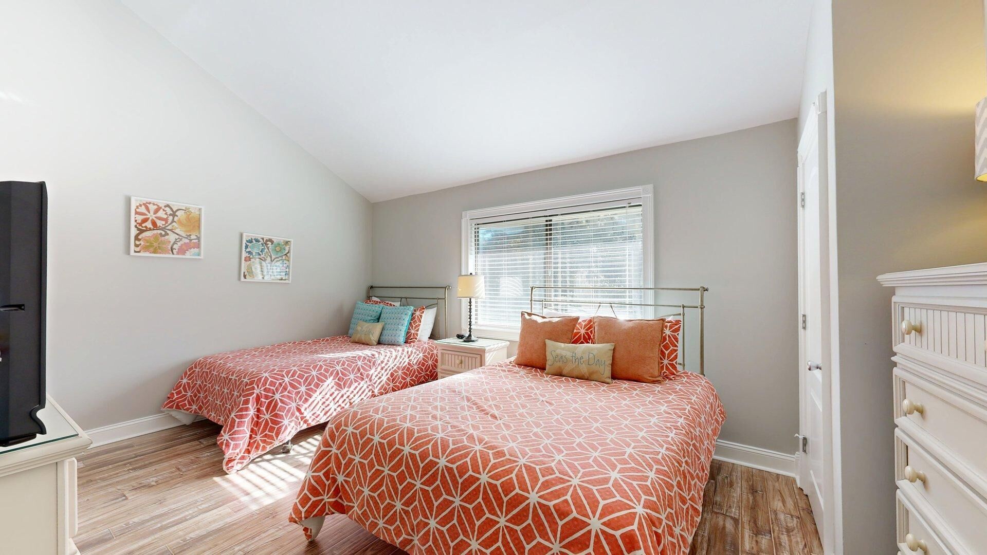 A bedroom with two beds, a dresser, a nightstand, and a window with blinds.
