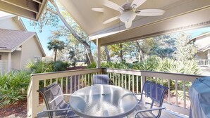 Un patio techado al aire libre con una mesa, sillas, ventilador de techo y vista a árboles y una casa.