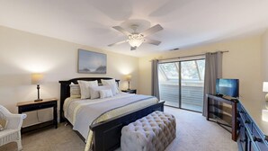 Un dormitorio con cama, ventilador de techo, televisor y ventana con cortinas.