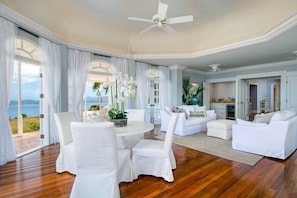 Amplia sala de estar con vista al mar, un comedor con mobiliario blanco y una zona de cocina.