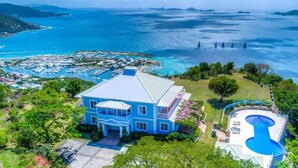 Un'ampia casa con piscina, circondata da un lussureggiante verde e vista mare.