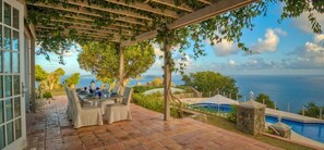 Un patio cubierto con una mesa lista para comer, una piscina y vistas al mar.