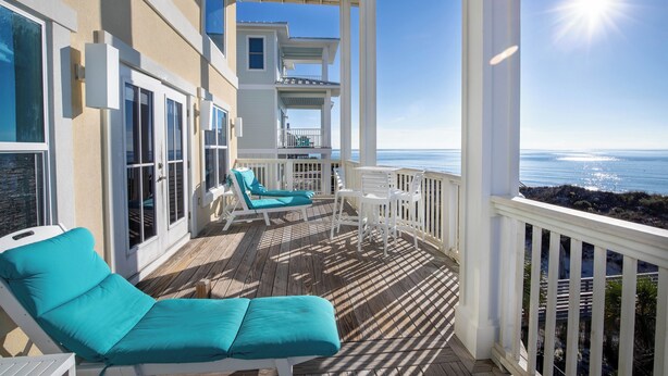 Ein Balkon mit zwei türkisfarbenen Liegestühlen, einem kleinen Tisch und Blick auf das Meer.